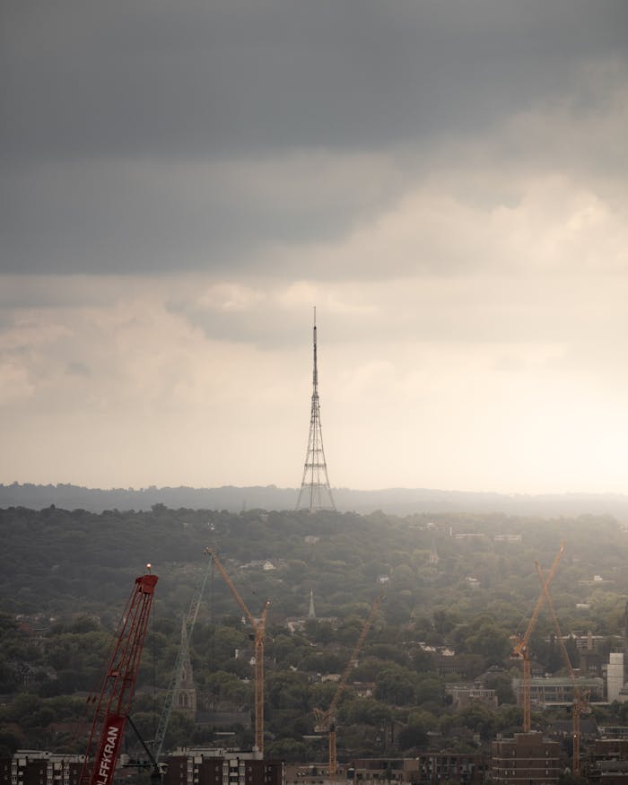 Aerial view of a television tower surrounded by cranes during dawn with clouded sky.