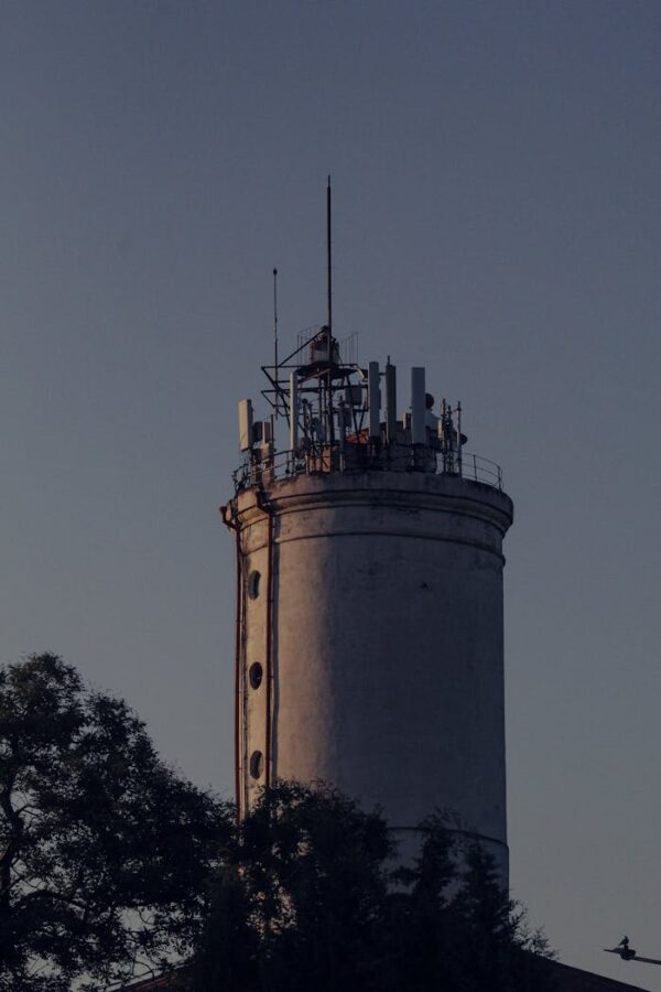 Close-up of an industrial tower with antenna installations at sunset, surrounded by trees.