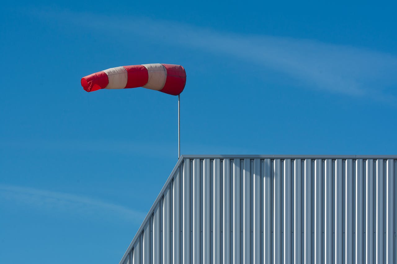 A red and white windsock on a corrugated rooftop under a clear blue sky.