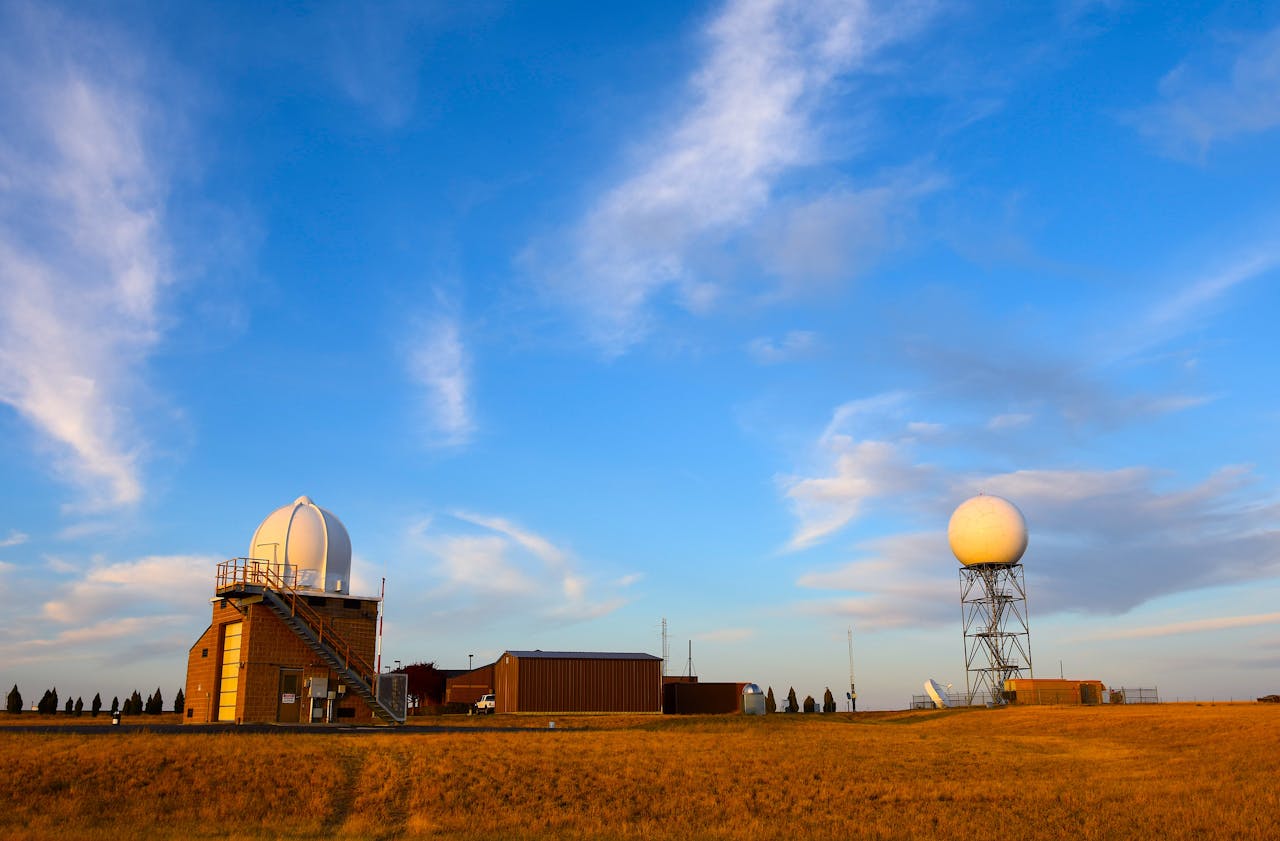 Weather radar station set in a field with a clear blue sky and scattered clouds, showcasing meteorological technology.