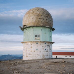 A weather radar tower on a mountain summit with a clear sky background.