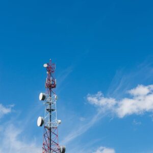 A tall telecommunication tower stands against a backdrop of clear blue sky with white clouds, symbolizing modern technology.